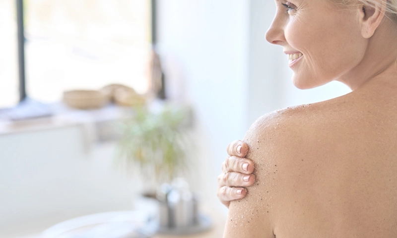 Back view of woman applying exfoliating scrub after shower.