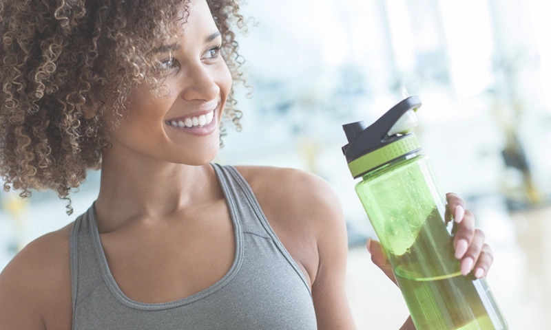 Beautiful woman holding clear green water bottle wearing a workout tank top