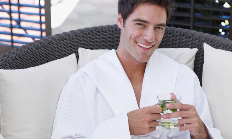 Male relaxing in a spa robe holding water infused with mint
