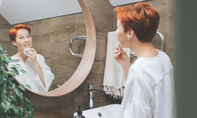 woman looking in mirror, taking care of skin