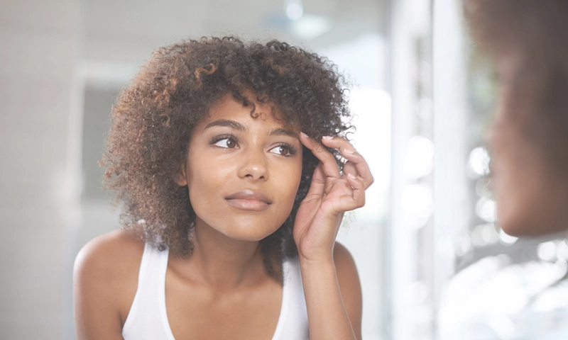 woman looking in mirror at shape of her brows