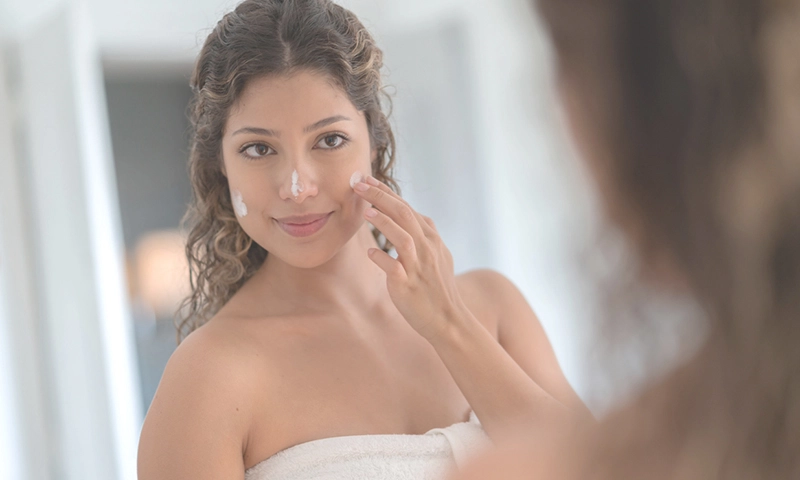 Portrait of a beautiful woman in the bathroom applying sunscreen on her face and looking in the mirror