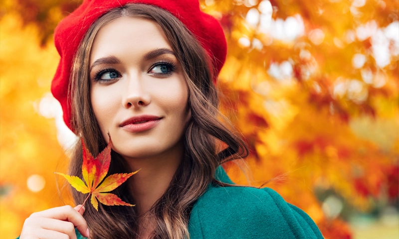 beautiful woman holding a fall leave and wearing a red hat