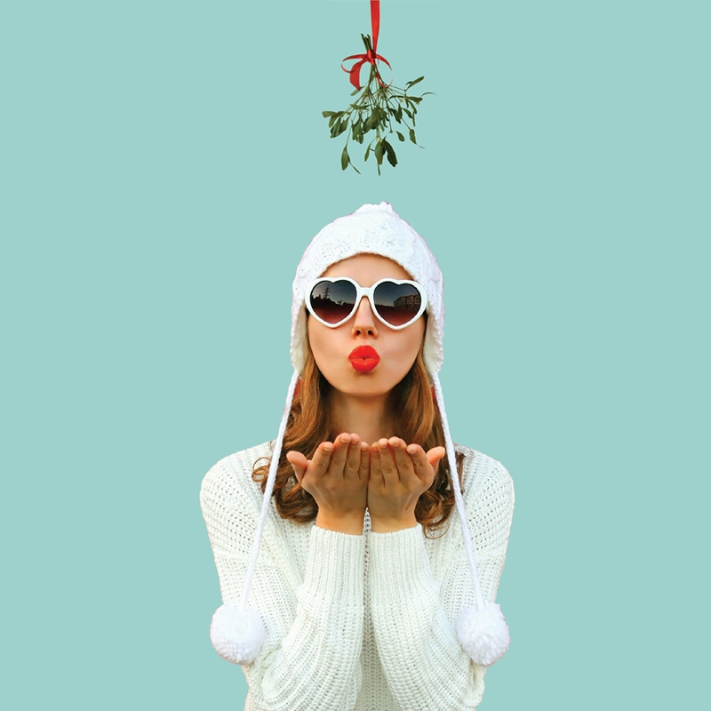 Beautiful woman blowing kiss below mistletoe